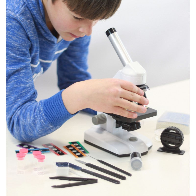 Criança a ajustar o foco do Buki Microscópio 1000x HD, com acessórios de preparação de amostras em volta.
