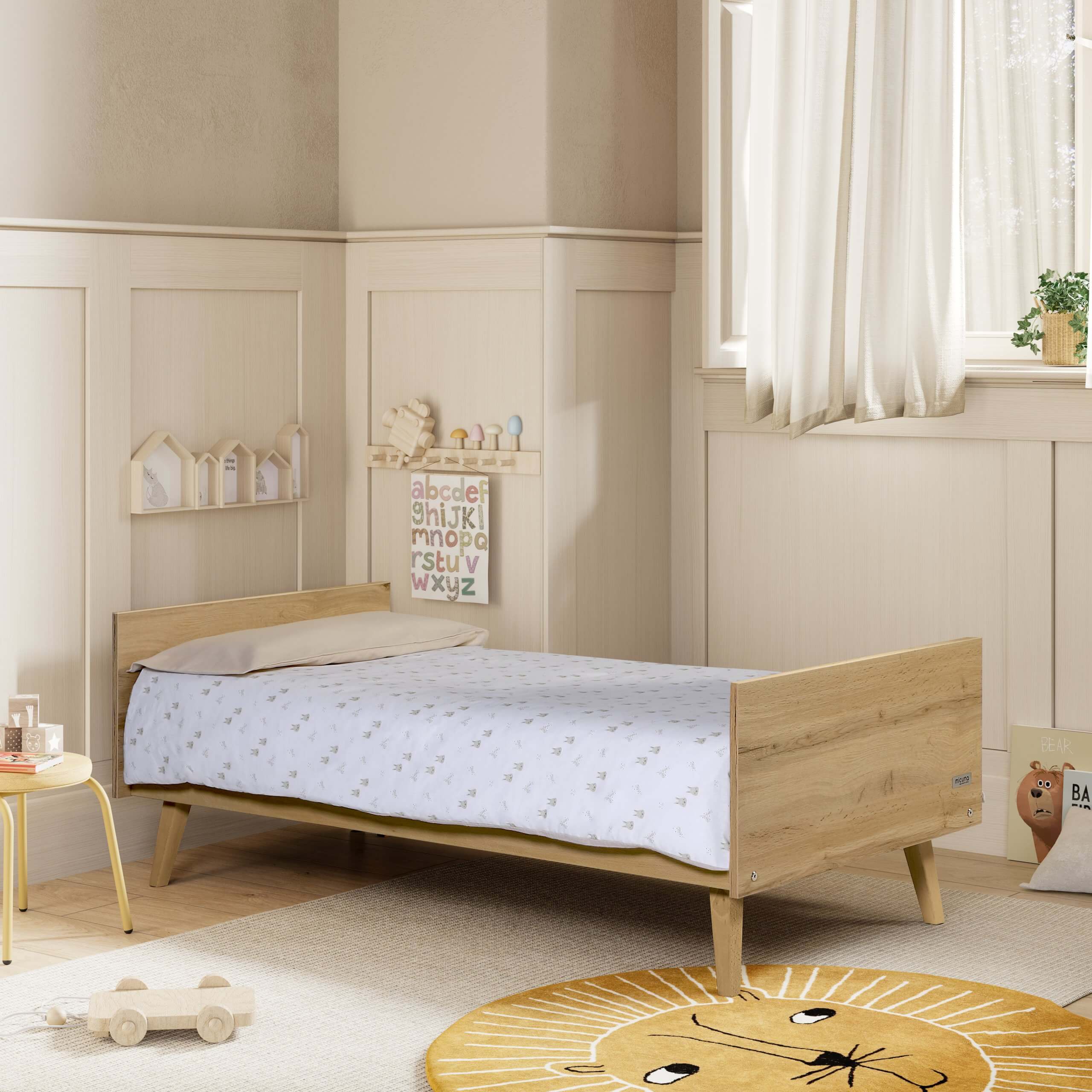 Berço Micuna Big Martha 140x70 convertido em caminha infantil num quarto moderno com tapete de leão e prateleiras decorativas.