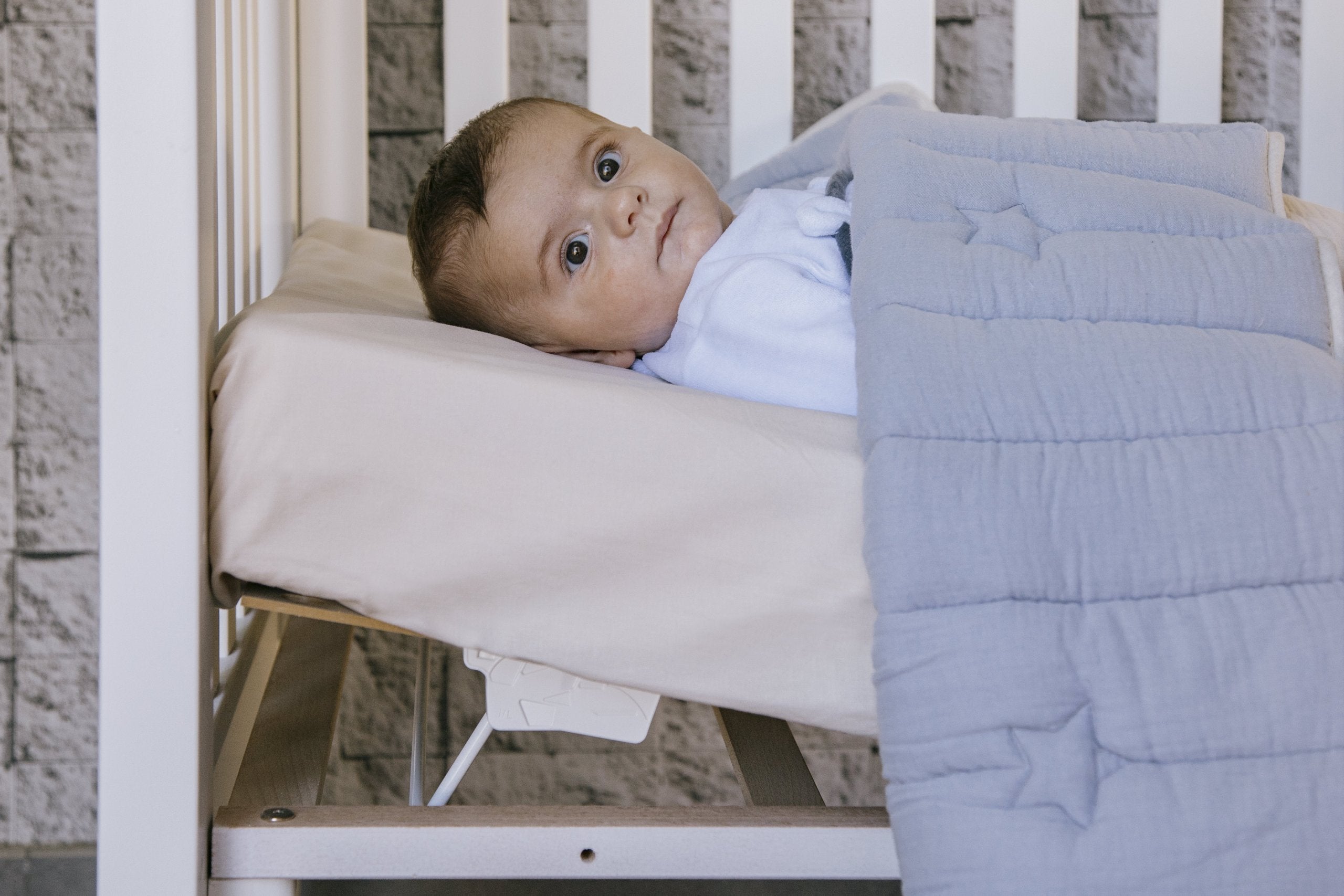 Bebé deitado confortavelmente num colchão Micuna inclinado dentro de um berço, demonstrando o Relax System em uso.