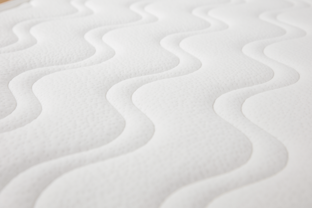 Vista aproximada da superfície de um colchão viscoelástico Micuna branco, destacando o padrão ondulado e a textura do tecido respirável.