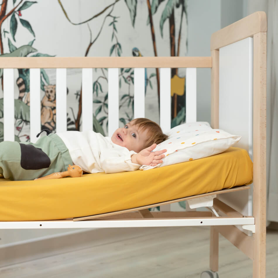 Bebé sorridente em berço com estrado Micuna reclinável 120x60, mostrando o Relax System para conforto e saúde.