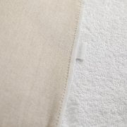 Detalhe do tecido da forra de fraldário, mostrando a costura entre a parte exterior bege/creme e a superfície interior branca texturada (algodão/bambu).