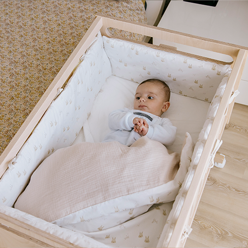 Bebé a dormir calmamente numa minicuna de madeira clara com o Kit Micuna nórdico e protector de 80x50, padrão de coelhos.