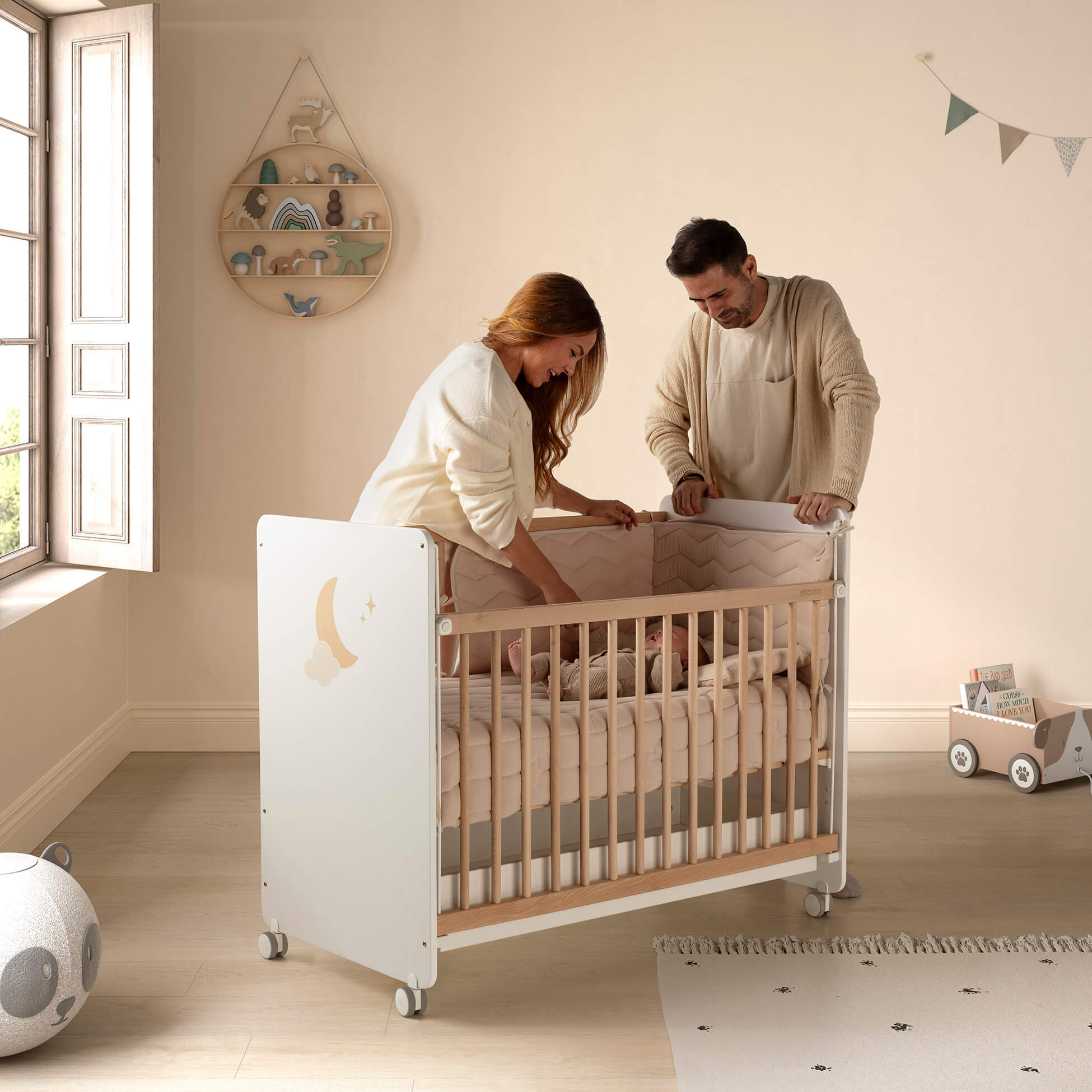 Pais interagem com bebé no berço Micuna Lupita 120x60 branco e madeira, com decoração de lua.