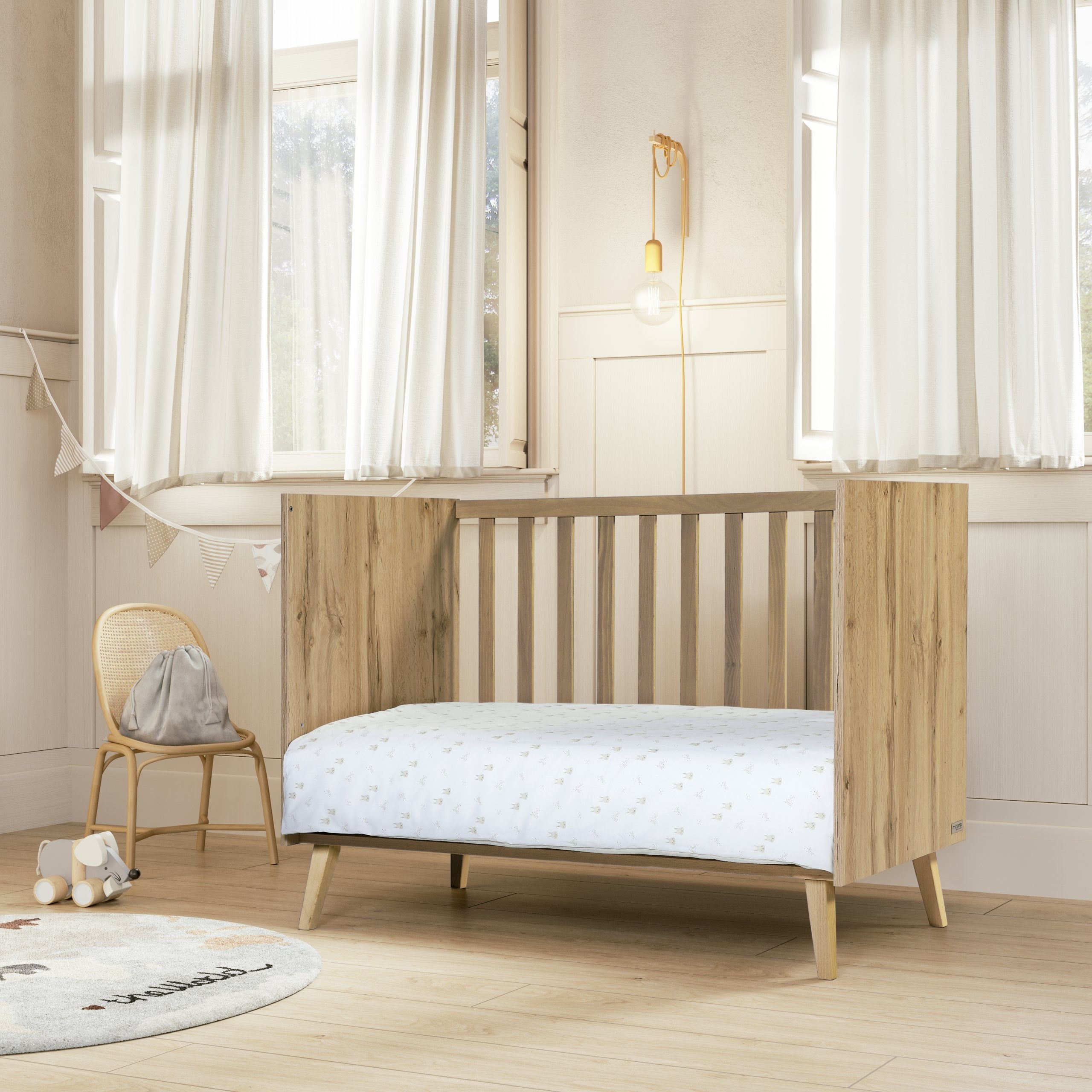 Berço Micuna Martha Big 140x70 em madeira de carvalho num quarto infantil moderno com cortinas brancas, tapete redondo e brinquedos.