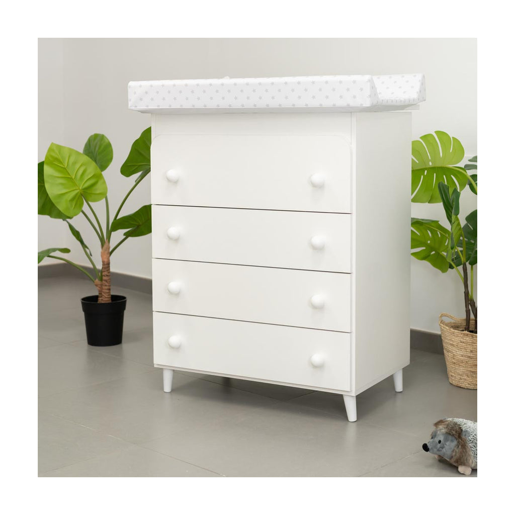 Cómoda Micuna branca com quatro gavetas, colchão muda-fraldas e pés de conversão, num quarto moderno com plantas.