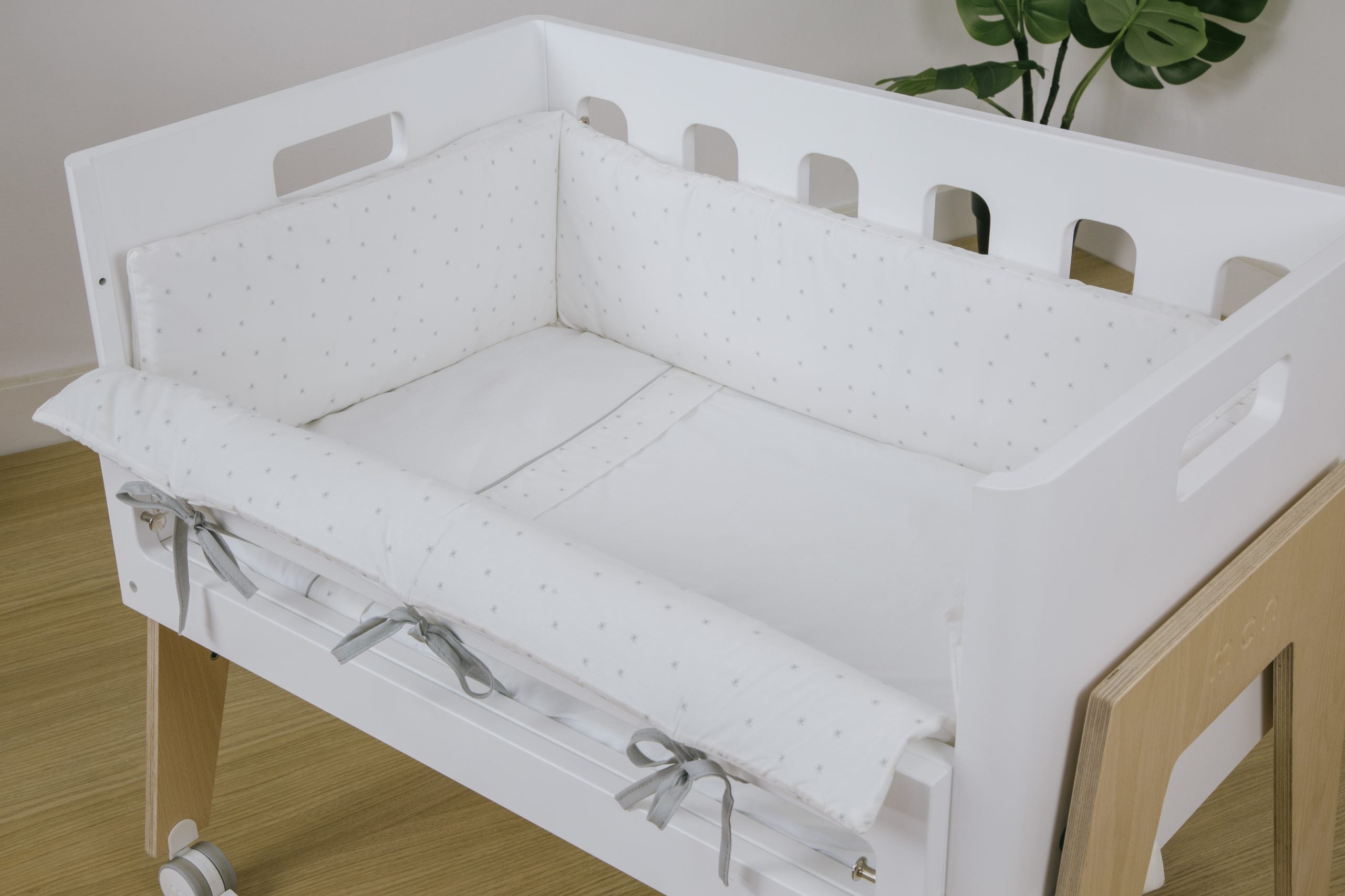 Vista aproximada do protetor de berço com laços cinzentos, mostrando o padrão de estrelas do kit Micuna Shine.