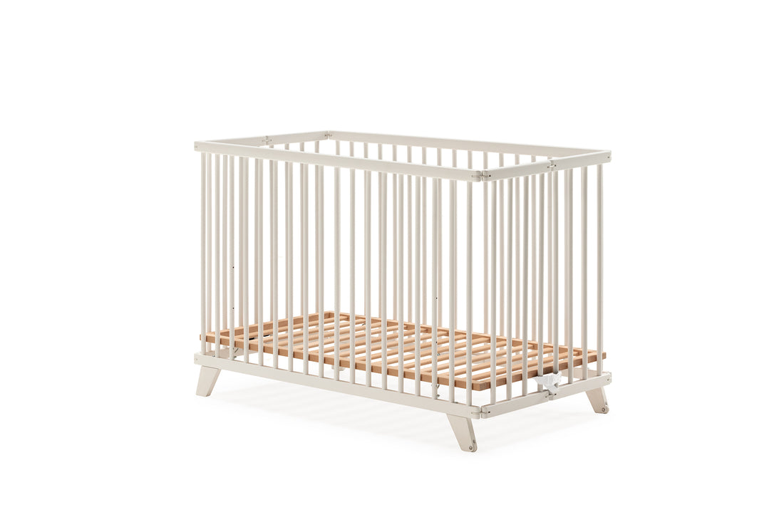 Berço Micuna Simona 120x60 branco num quarto de bebé moderno com poltrona, janela e decoração suave.