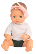 Boneca bebé caucasiana Miniland de 32cm, sentada, com cabelo louro, olhos azuis e laço rosa na cabeça.