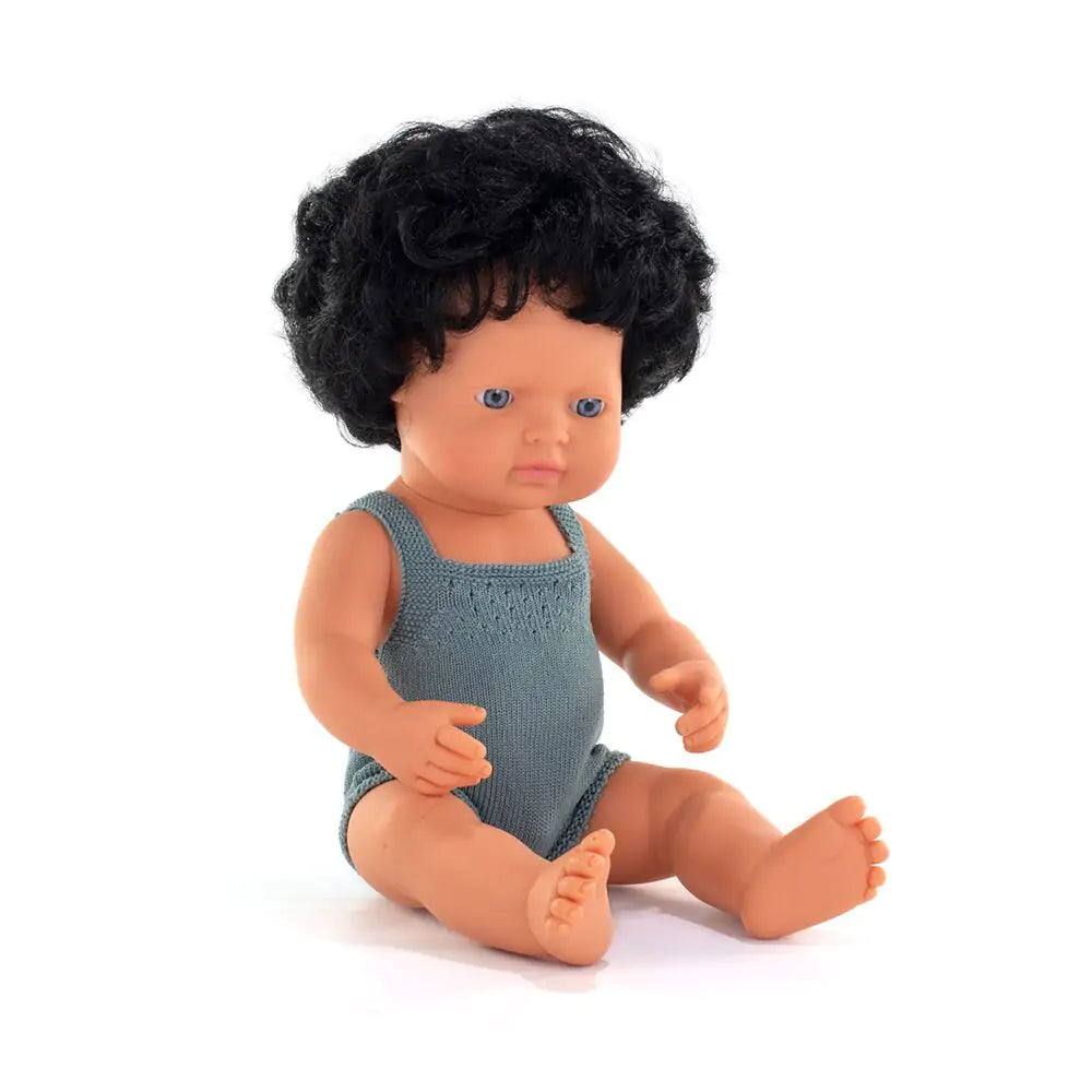 Boneco bebé Miniland caucasiano de 38cm, sentado, com cabelo preto encaracolado e olhos azuis, vestido com um macacão de malha azul.
