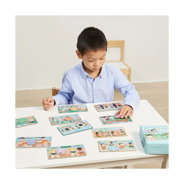 Criança sentada à mesa a brincar atentamente com o Miniland Jogo de Emotiduos, organizando as peças de puzzle e as fichas de emoção.