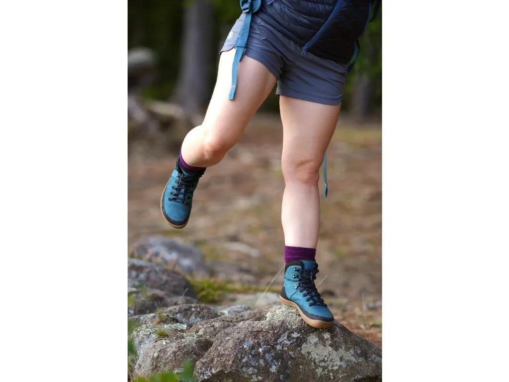 Mulher caminhando em trilha rochosa com botas barefoot MITU femininas em azul petróleo, um calçado ideal para trekking.

