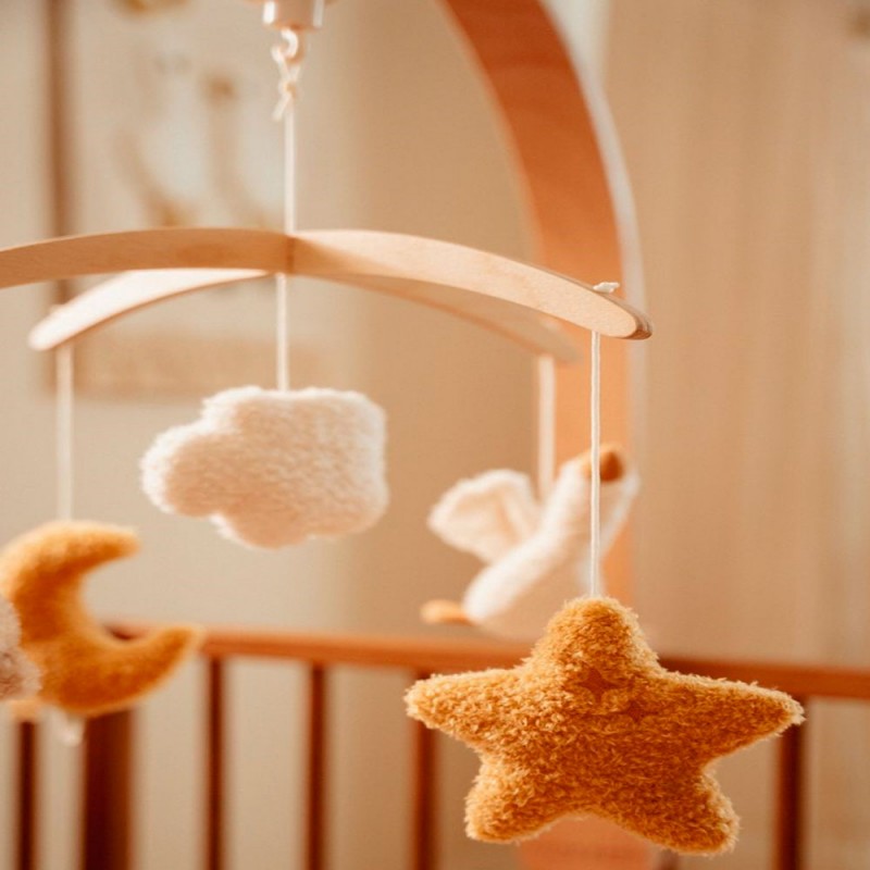 Detalhe das figuras de peluche macias do móbile (estrela amarela, lua, nuvem, ganso) em foco, mostrando a textura felpuda.