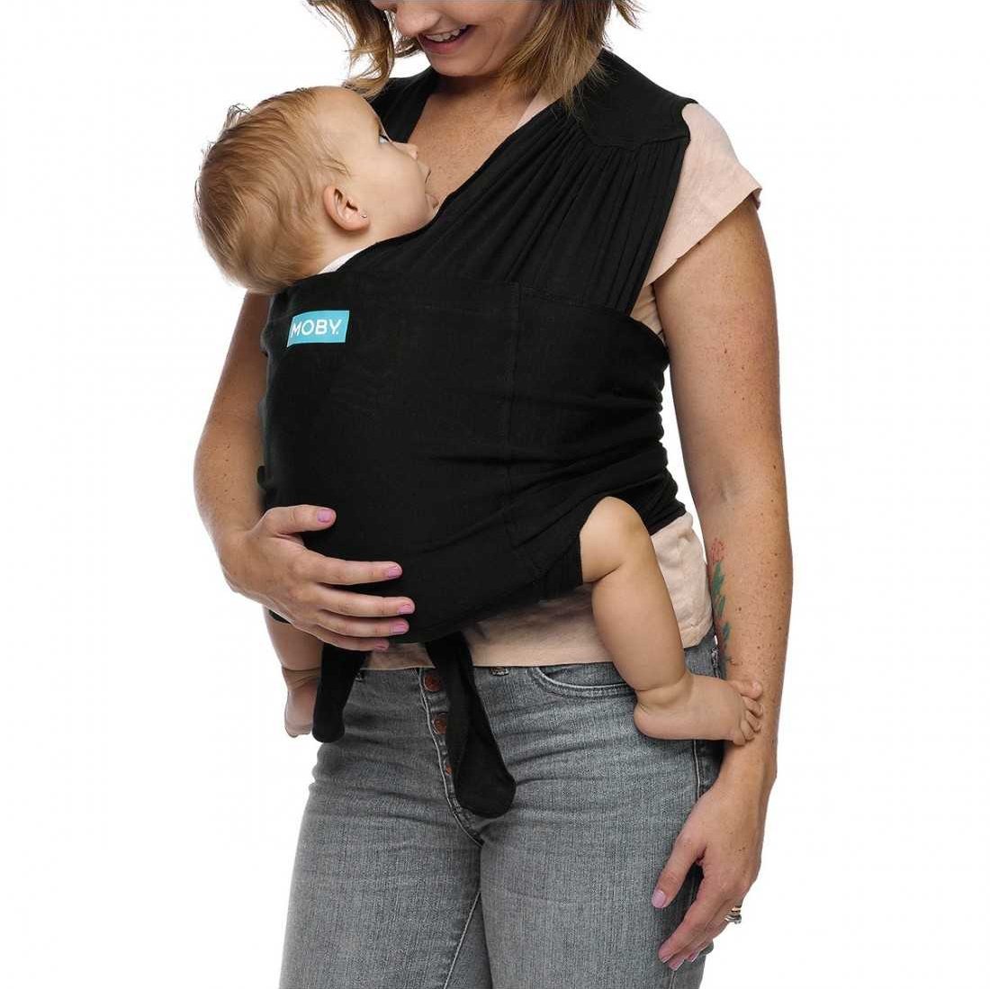 Mulher de lado a ajustar a Mochila de Pano Elástico Moby FIT Black com um bebé no colo.