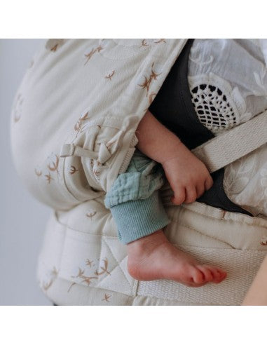 Mulher de pé com uma blusa branca, carregando um bebé num porta-bebés Fidella Fusion Evolutiva Baby Cotton Flower Pale Grey. O bebé está seguro e confortável no porta-bebés ajustado, com a cabeça encostada ao peito da mãe.