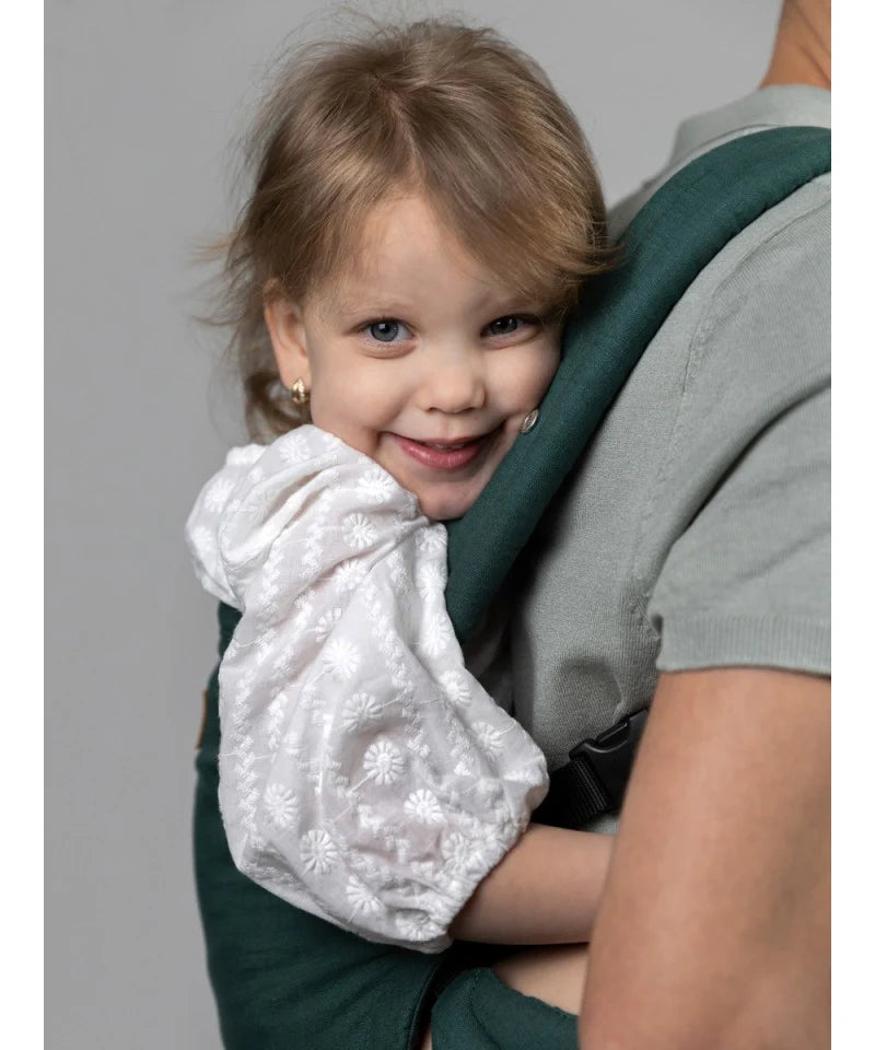 Close-up de uma criança sorrindo enquanto é carregada na Mochila Isara Elite Ajustável Evergreen Linen, mostrando o conforto do bebé.