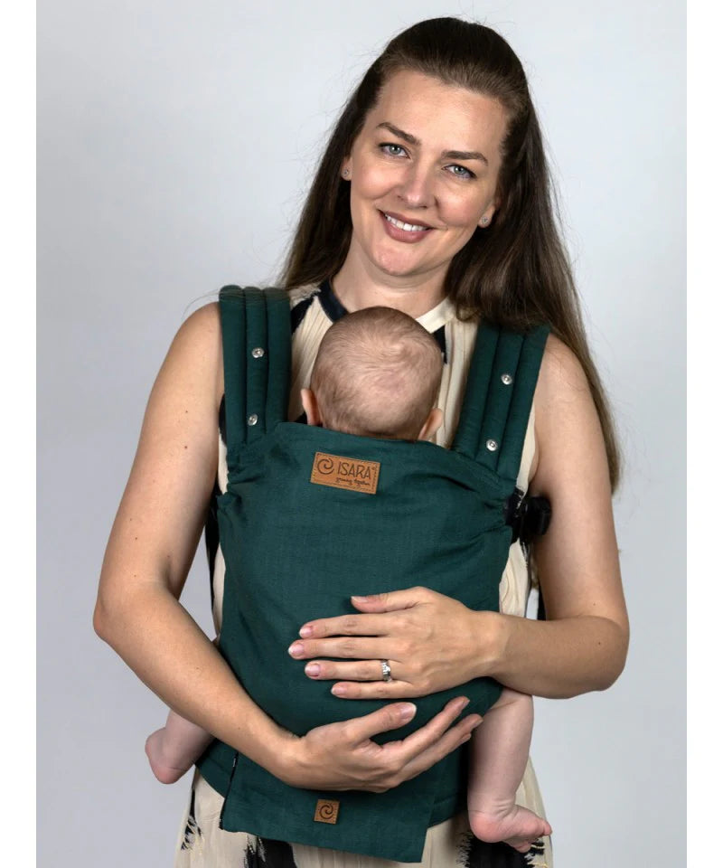 Uma mãe sorridente a usar a Mochila Isara Elite Ajustável Evergreen Linen, a carregar um bebé confortavelmente na posição frontal.