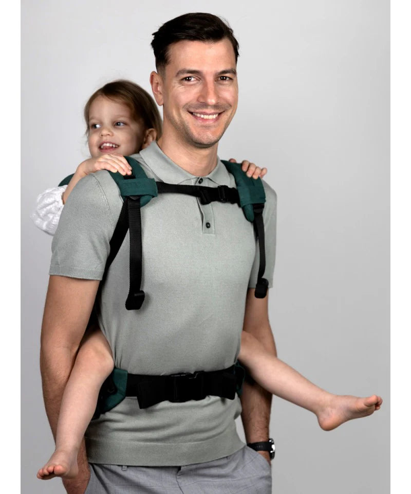 Um pai sorridente a carregar uma criança na Mochila Isara Elite Ajustável Evergreen Linen, numa posição de costas, mostrando o ajuste e o conforto.