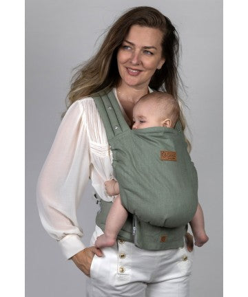 Mãe sorridente transporta um bebé adormecido na mochila ergonómica Isara ELITE Ajustável cor Sage Green Linen, tecido jacquard.