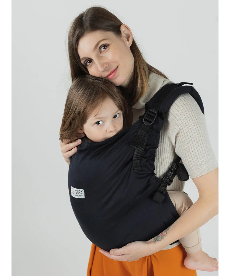 Mulher a usar a mochila Isara Toddler Preschooler Noire com uma criança na posição frontal, vista frontal, detalhe do tecido.