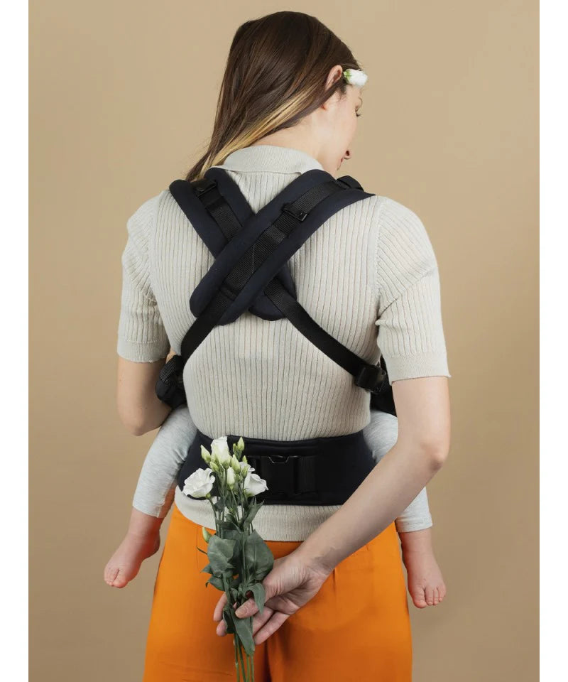 Mulher a usar a mochila Isara Toddler Preschooler Noire com uma criança às costas, vista traseira.