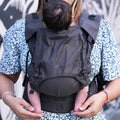 Mãe usa a mochila Neko Switch Shadow cinzenta para transportar um bebé pequeno, mostrando o ajuste ergonómico e o suporte nas costas.