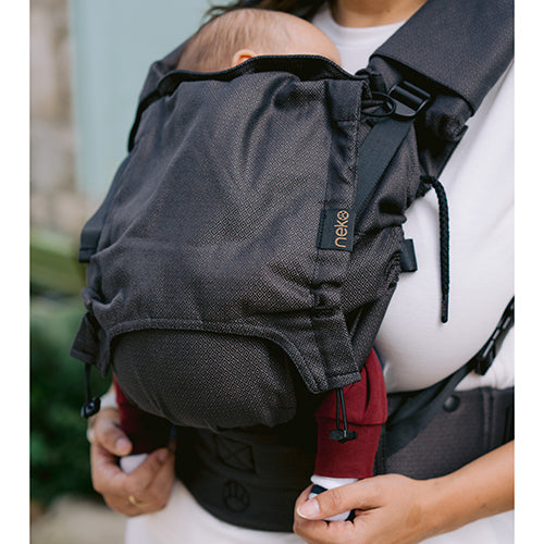 Detalhe da mochila ergonómica Neko Switch Shadow escura, com um bebé a dormir, destacando o tecido e o logótipo Neko.