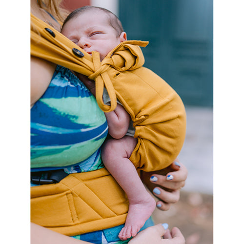 Bebé recém-nascido a dormir confortavelmente numa mochila de babywearing Neko Tiny cor mostarda, apoiado no peito do portador.