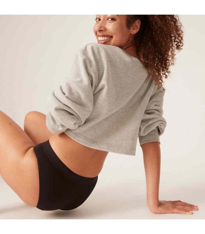 Modelo usando cueca menstrual Modibody preta, sentada e mostrando a cobertura traseira do produto.