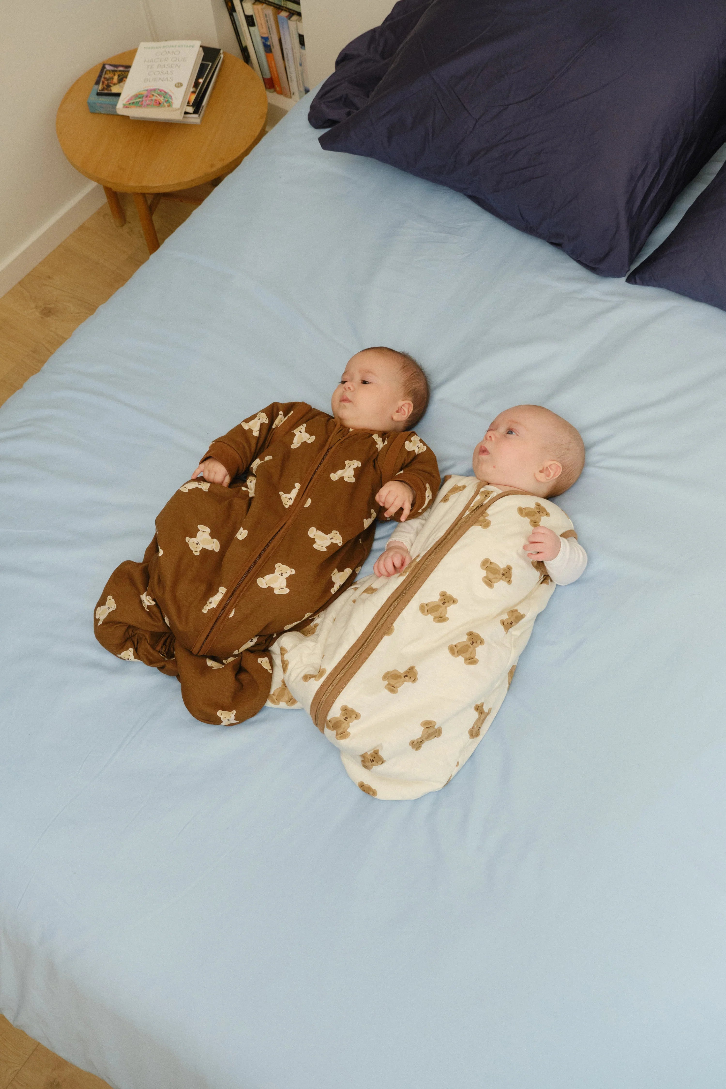 Dois bebés em sacos de dormir MolisandCo, um creme Teddy e outro castanho, deitados na cama. Conforto e segurança.