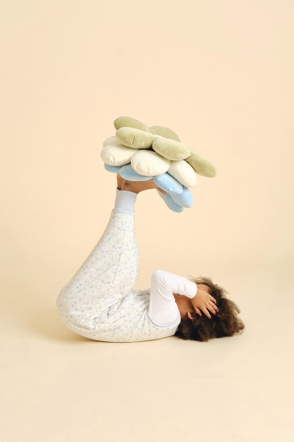 Criança deitada a brincar com almofadas florais, vestindo o saco de dormir com pés MolisandCo, demonstrando liberdade de movimento.