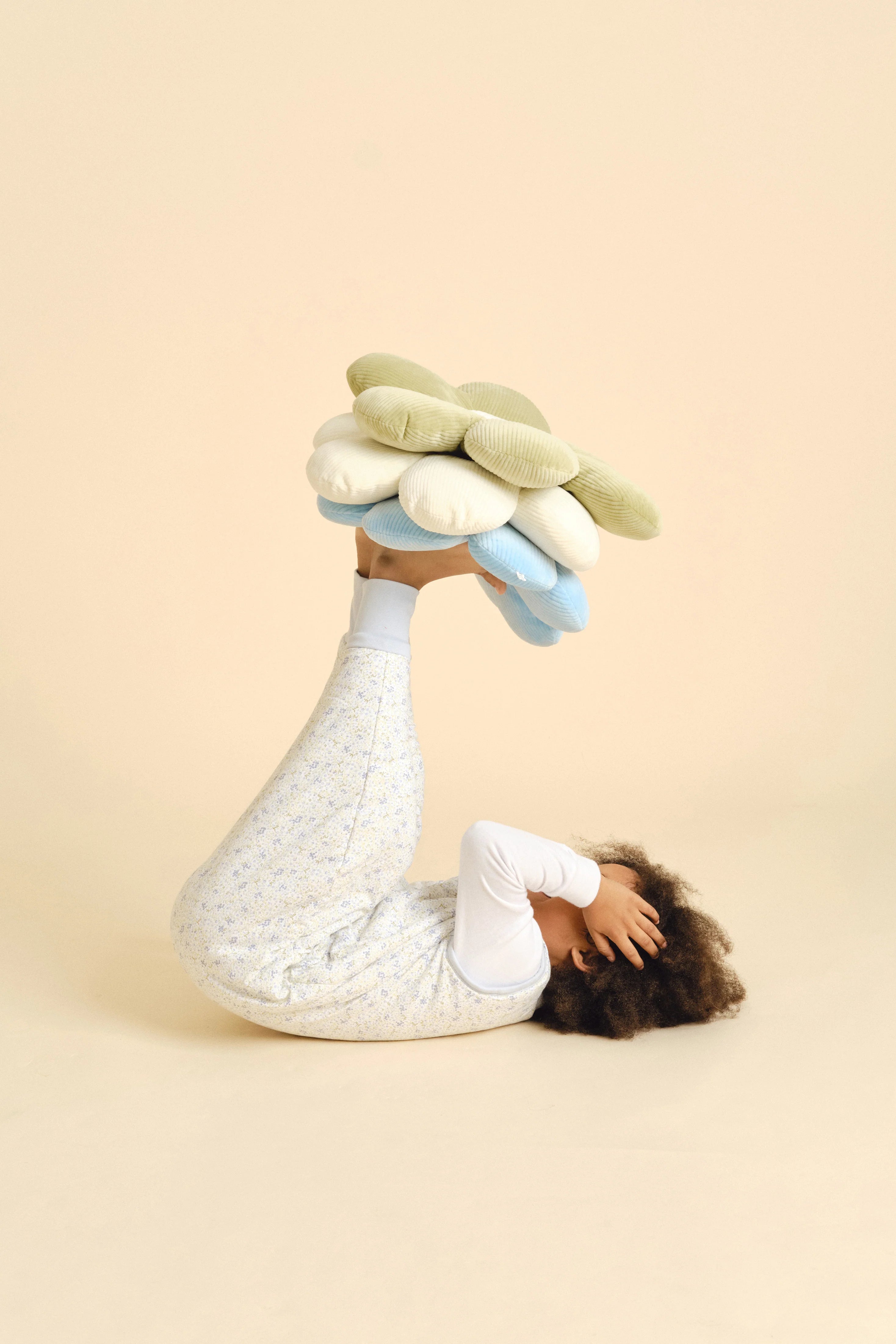 Criança deitada a brincar com almofadas florais, vestindo o saco de dormir com pés MolisandCo, demonstrando liberdade de movimento.