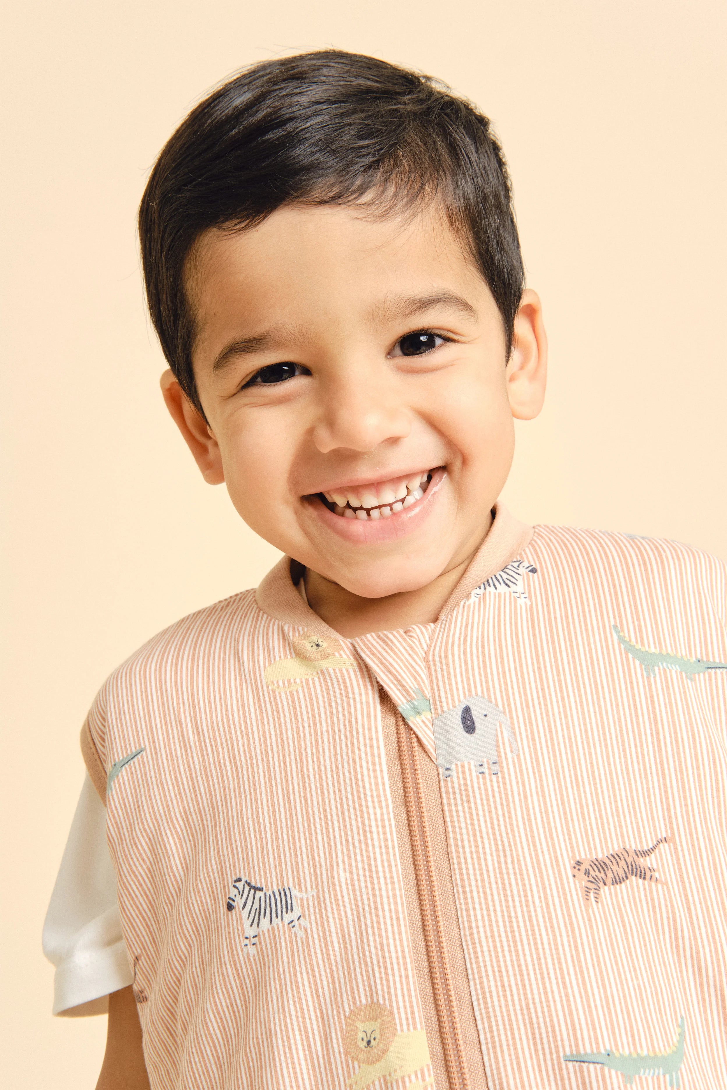 Menino sorridente com saco de dormir MolisandCo TOG 1.0 Jungle, padrão de animais, fecho frontal.
