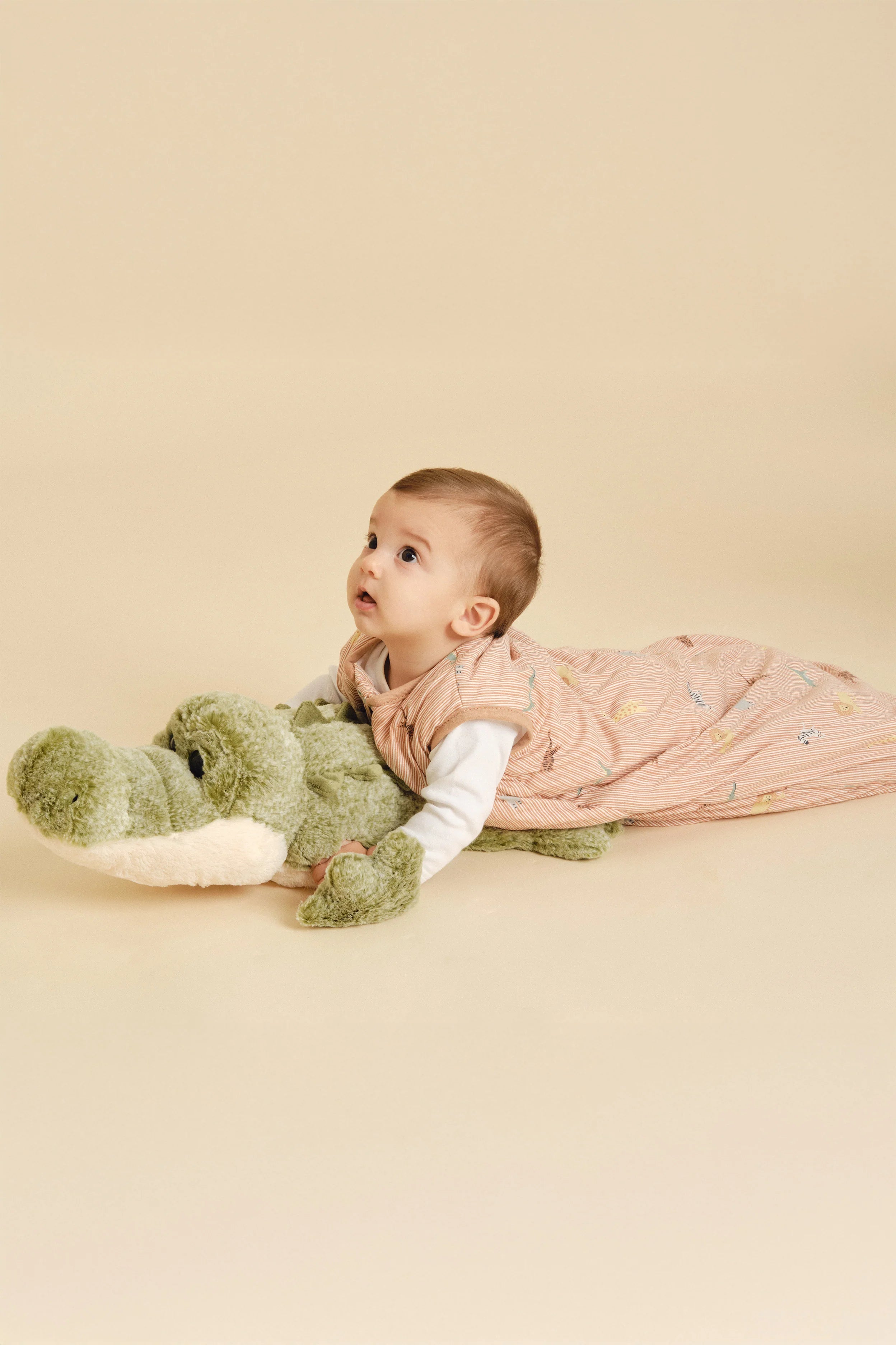 Bebé deitado de bruços, com saco de dormir MolisandCo TOG 1.0 Jungle e peluche crocodilo.