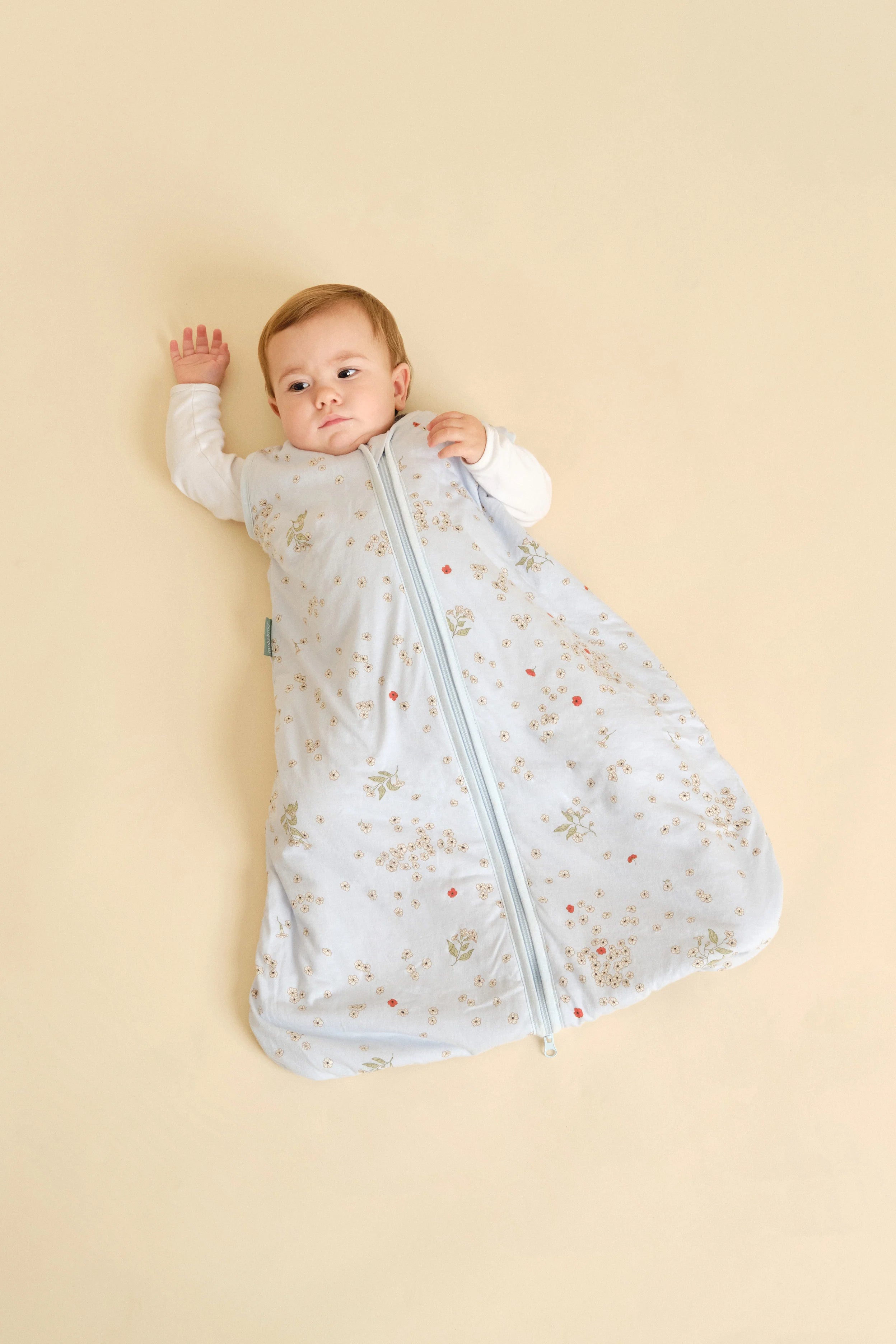 Bebé deitado de costas a usar saco de dormir MolisandCo TOG 1.0 "Poppy" azul. Ideal para um sono seguro e confortável.