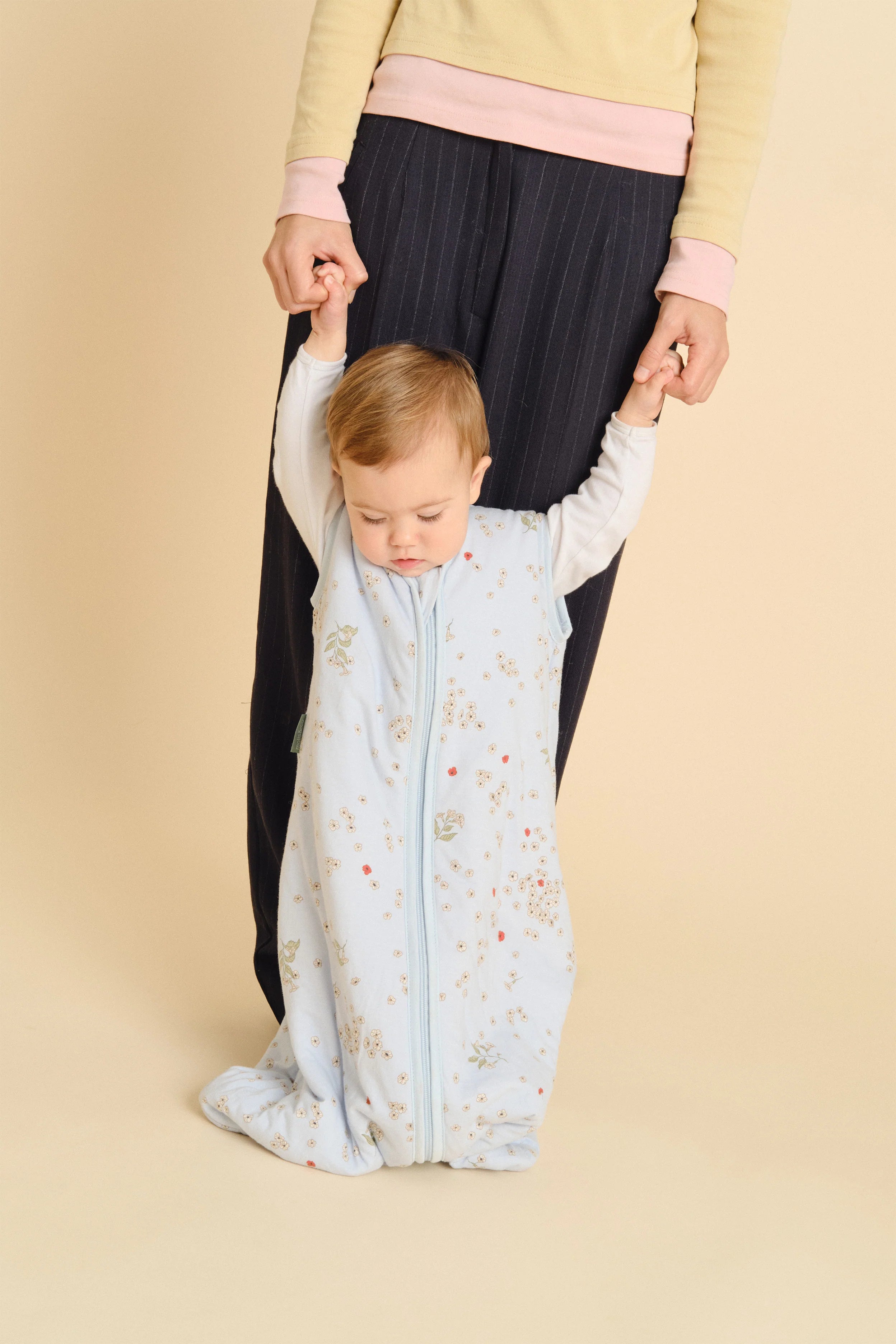 Bebé a usar saco de dormir MolisandCo TOG 1.0 "Poppy" azul, apoiado por um adulto. Mostra o ajuste e conforto.
