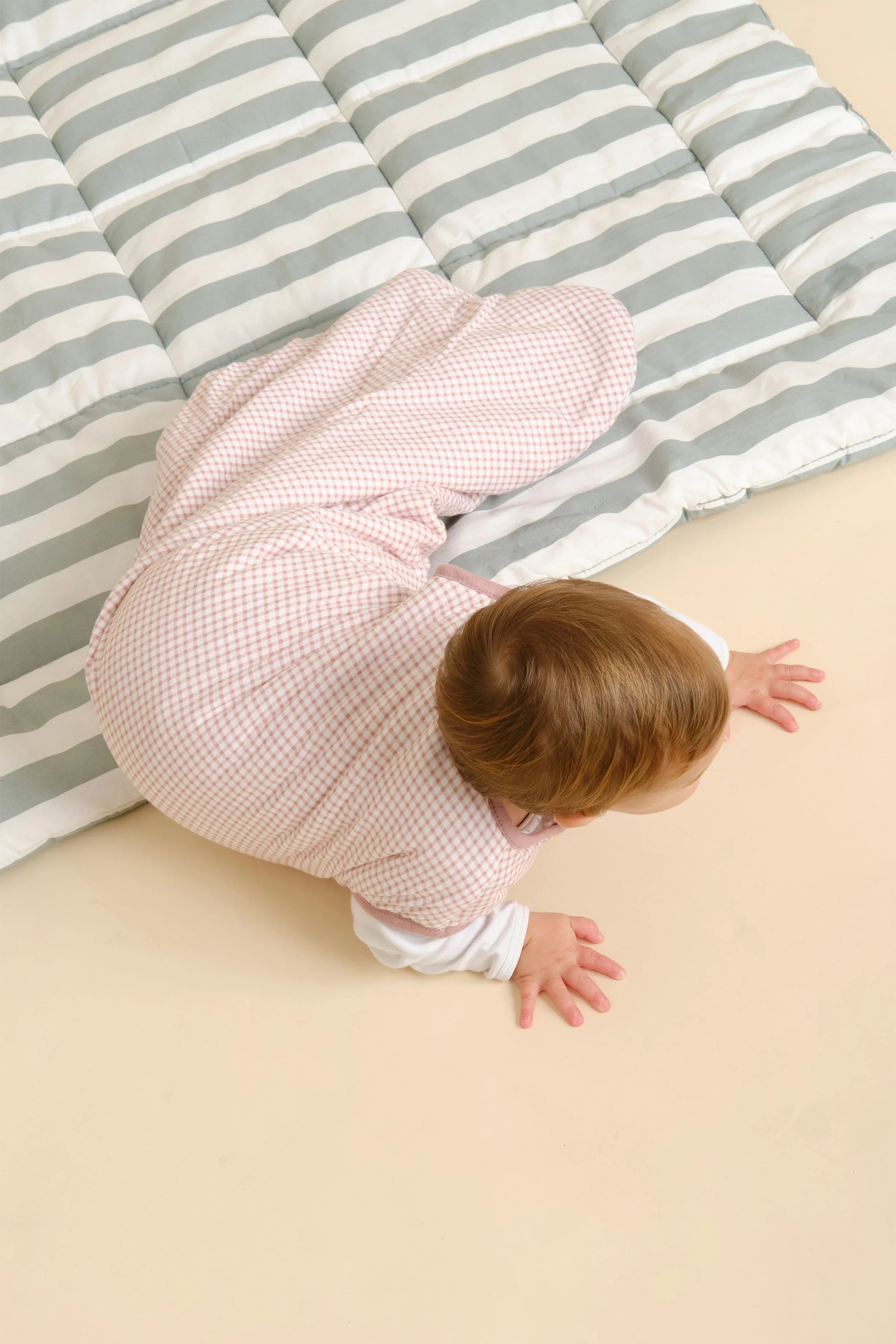 Bebé deitado de bruços no saco de dormir MolisandCo TOG 1.0 sem pés, padrão Vichy Pink, visto de cima.