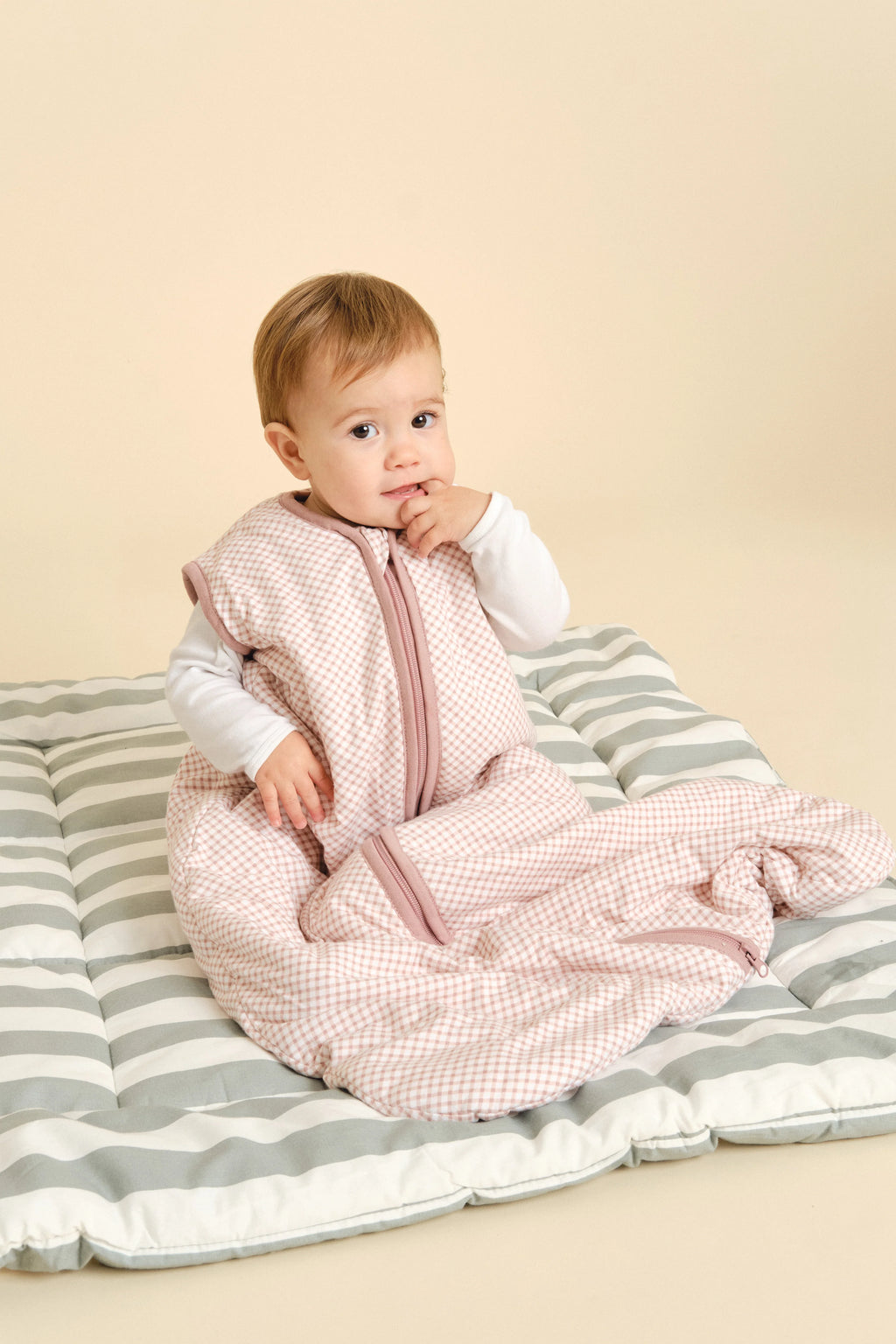 Bebé sentado confortavelmente no saco de dormir MolisandCo TOG 1.0 sem pés, padrão Vichy Pink, sobre um tapete.