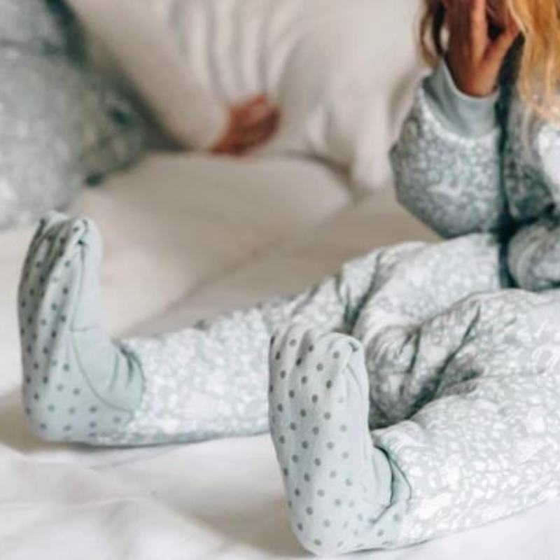 Detalhe dos pés do saco de dormir MolisandCo, mostrando as meias antiderrapantes com bolinhas cinzentas, enquanto a criança está sentada na cama.