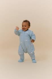 Bebé a gatinhar ou a dar os primeiros passos, sorridente, usando o saco de dormir MolisandCo TOG 2.5 com pés, destacando a mobilidade.