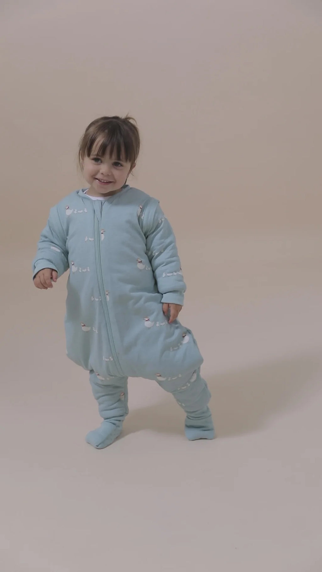 Criança sorridente vestindo o saco de dormir MolisandCo TOG 2.5 azul-claro com padrão de patos, mostrando a liberdade de movimento dos pés.