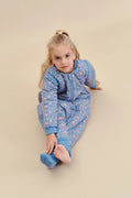 Criança loira sentada no chão, vestindo o saco de dormir MolisandCo TOG 2.5 azul com padrão floral "Wild Orchid".