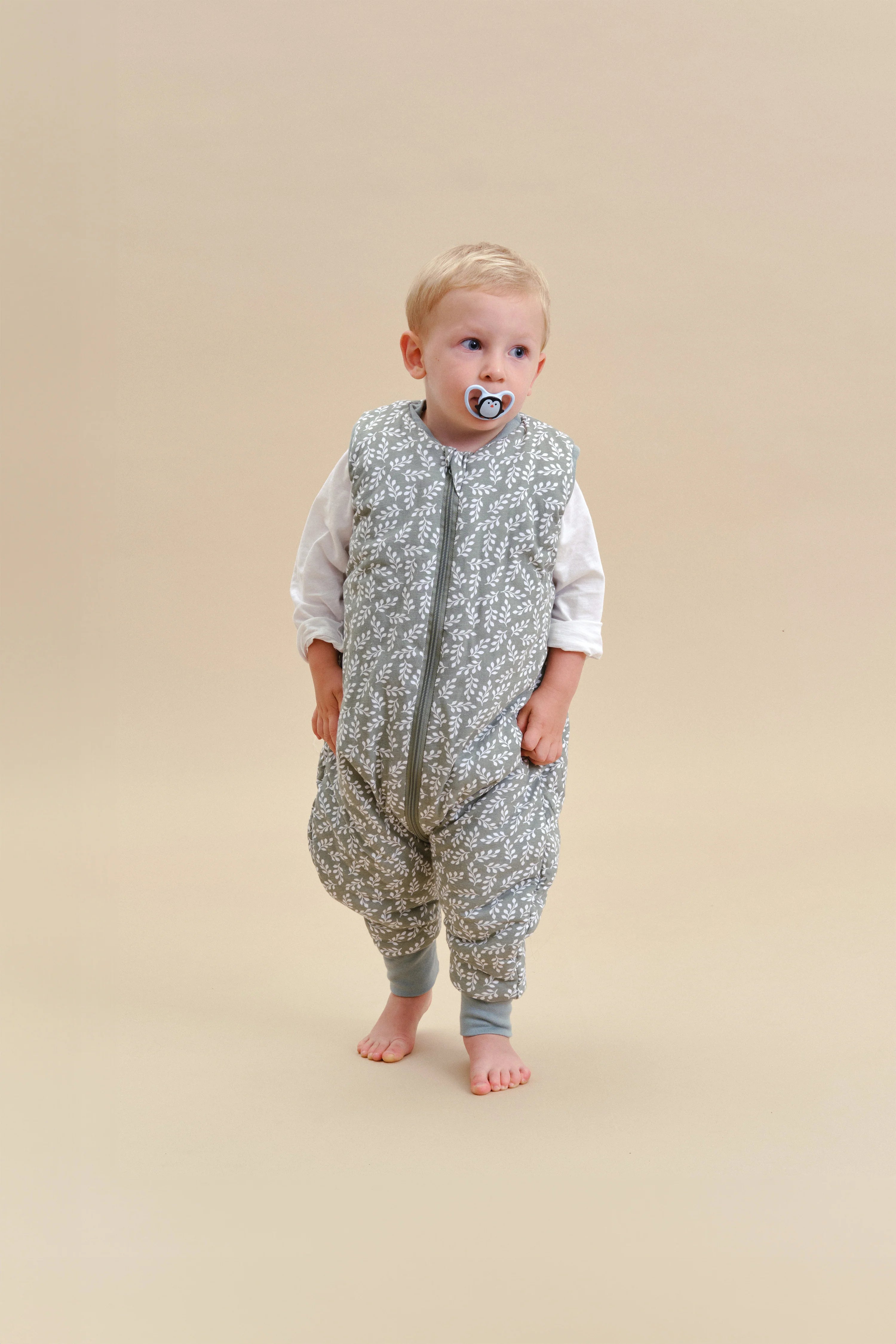 Bebé com saco de dormir MolisandCo Green Garden e chupeta, de pé. Design com pés para liberdade de movimento.