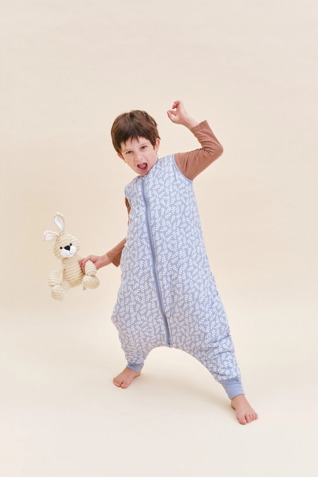 Criança feliz e ativa com saco de dormir MolisandCo TOG 2.5 Blue Garden e brinquedo de coelho.