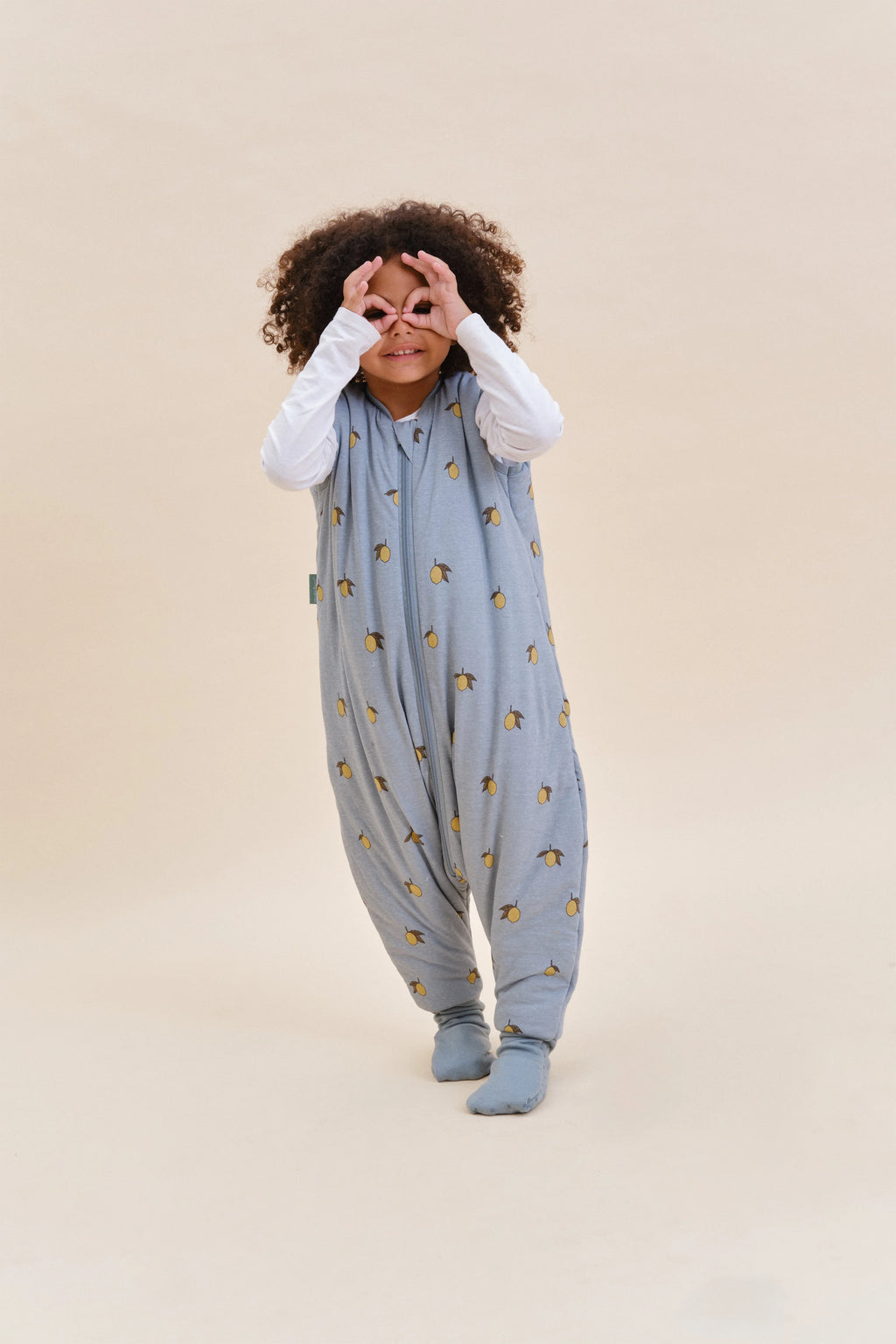 Menina feliz com saco de dormir MolisandCo TOG 2.5 com pés Colima, a brincar, demonstrando mobilidade e alegria.