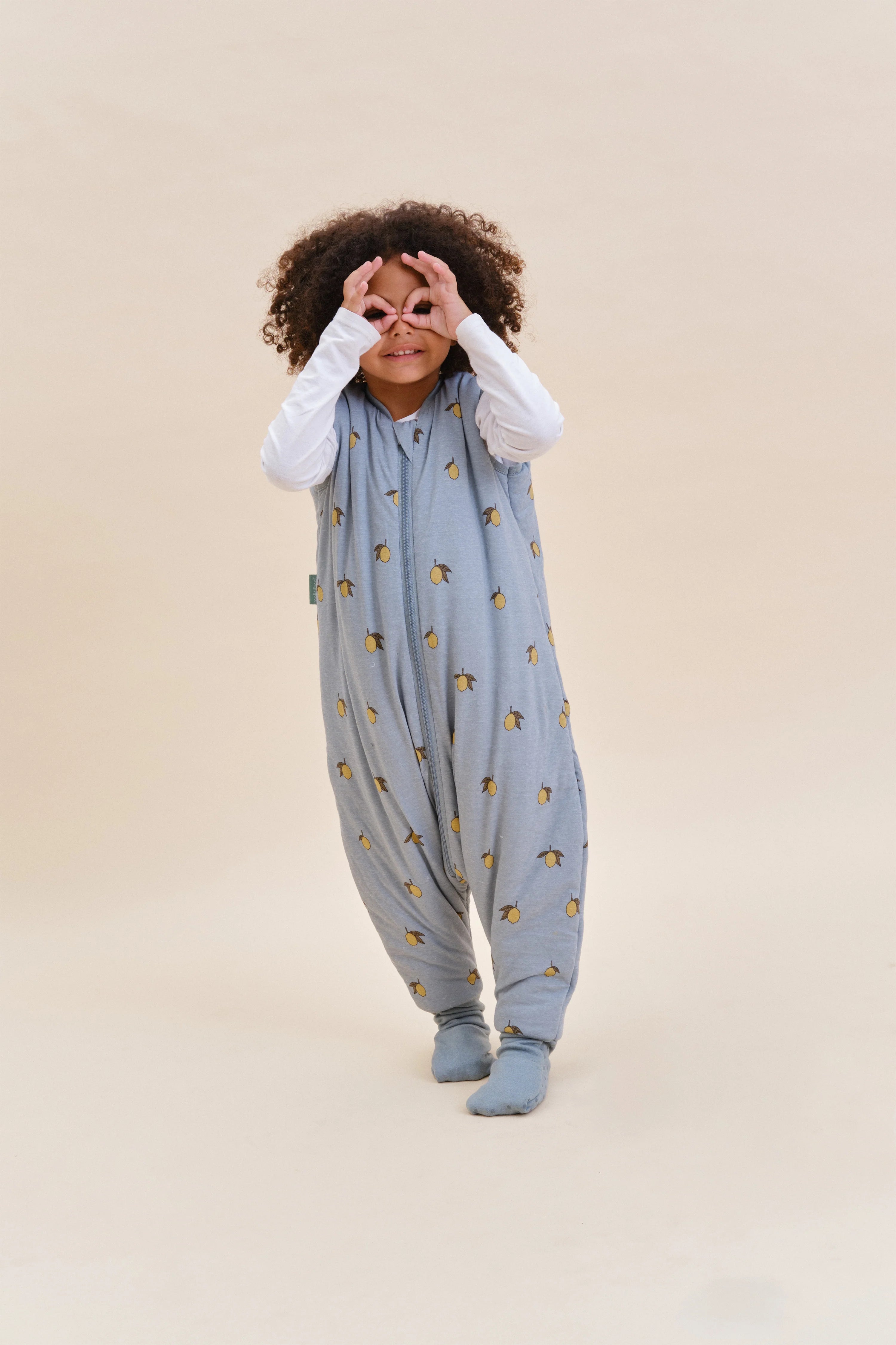 Menina feliz com saco de dormir MolisandCo TOG 2.5 com pés Colima, a brincar, demonstrando mobilidade e alegria.