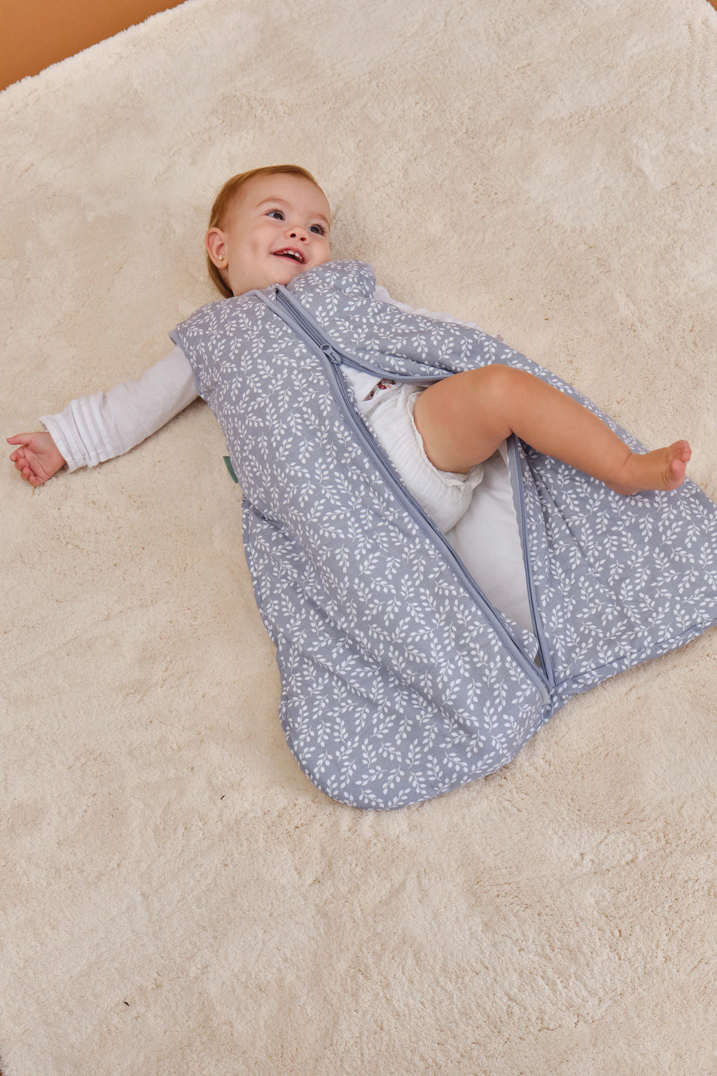 Bebé feliz no chão com saco de dormir MolisandCo TOG 2.5 Blue Garden aberto, mostrando a facilidade de uso.