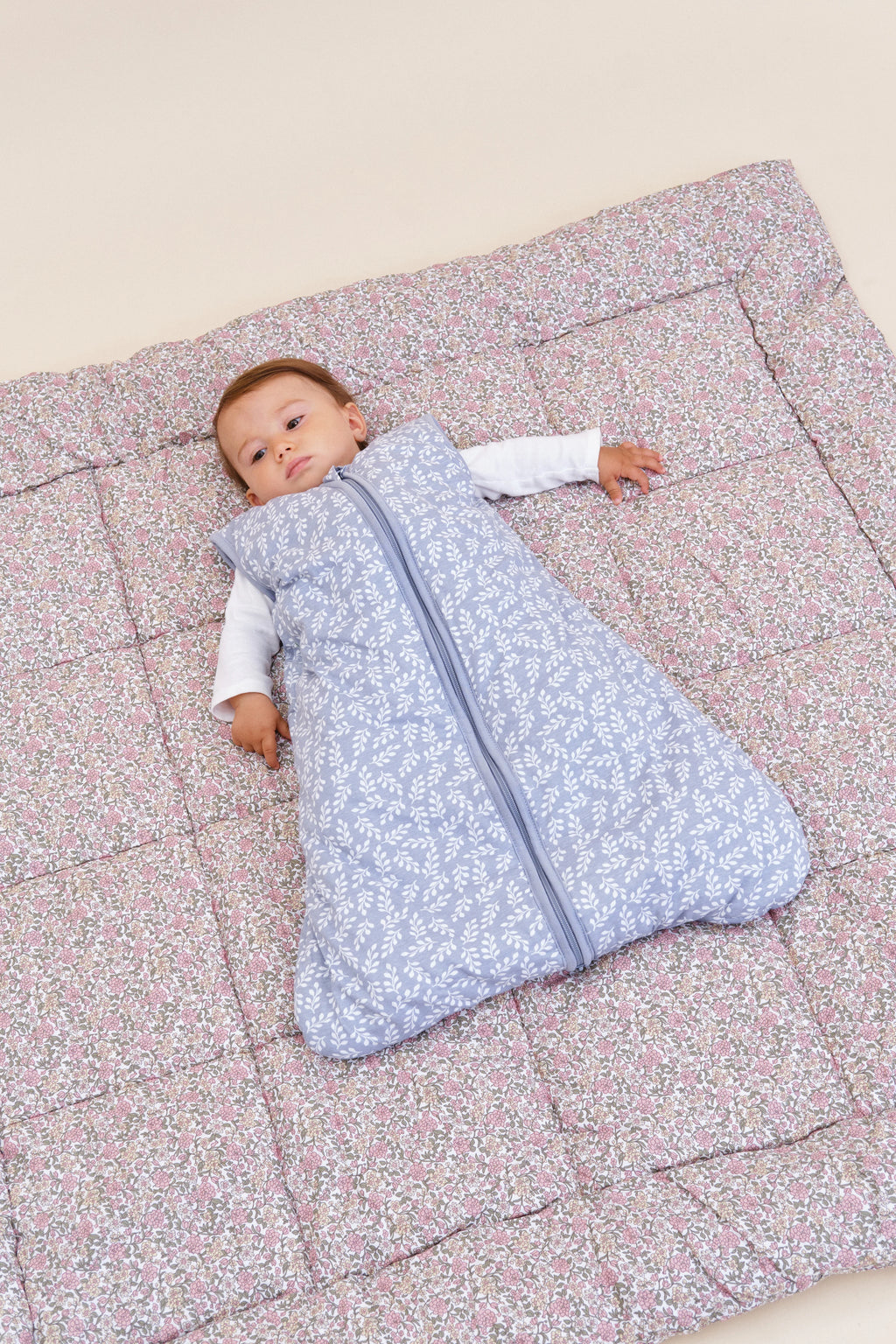 Bebé a dormir no saco MolisandCo TOG 2.5 Blue Garden sobre um edredão, realçando o conforto e segurança.