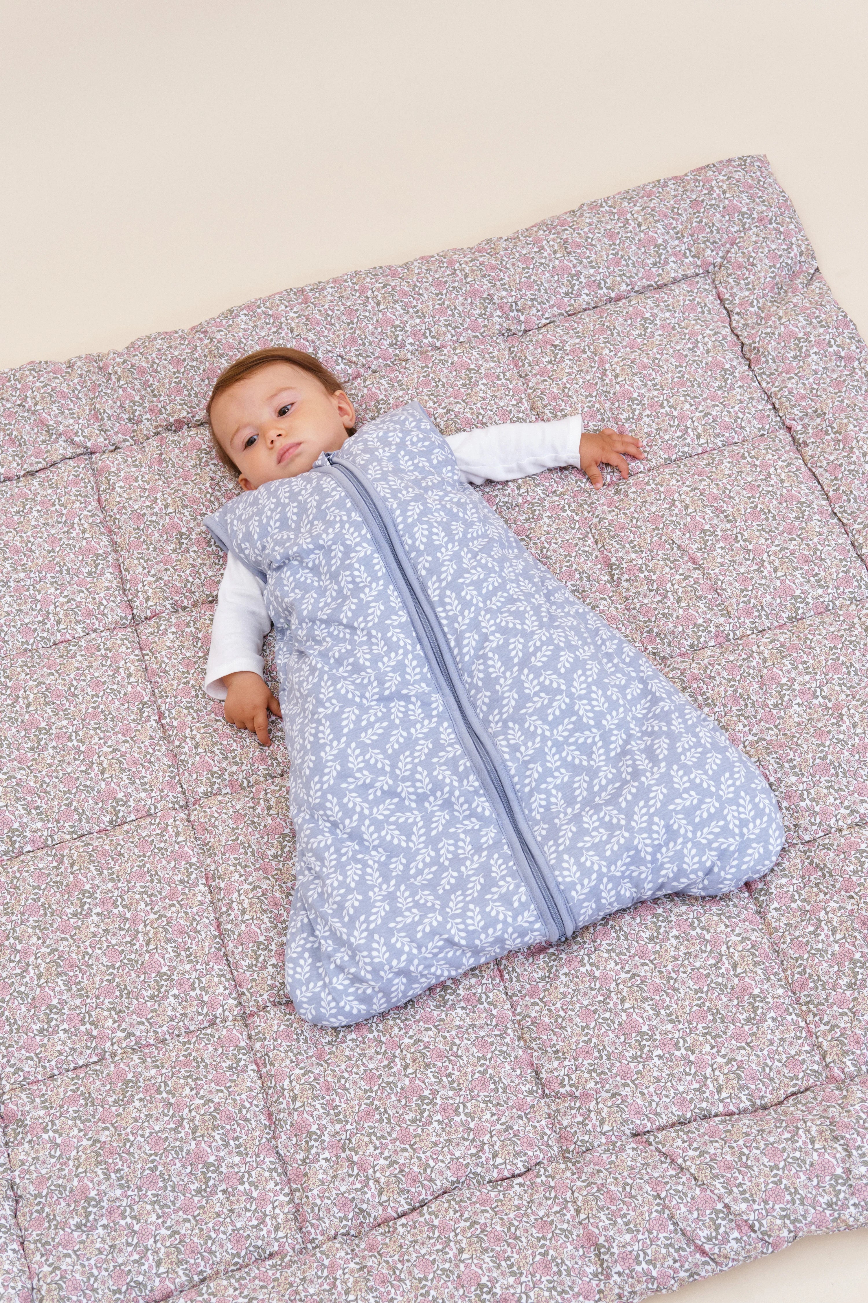 Bebé a dormir no saco MolisandCo TOG 2.5 Blue Garden sobre um edredão, realçando o conforto e segurança.
