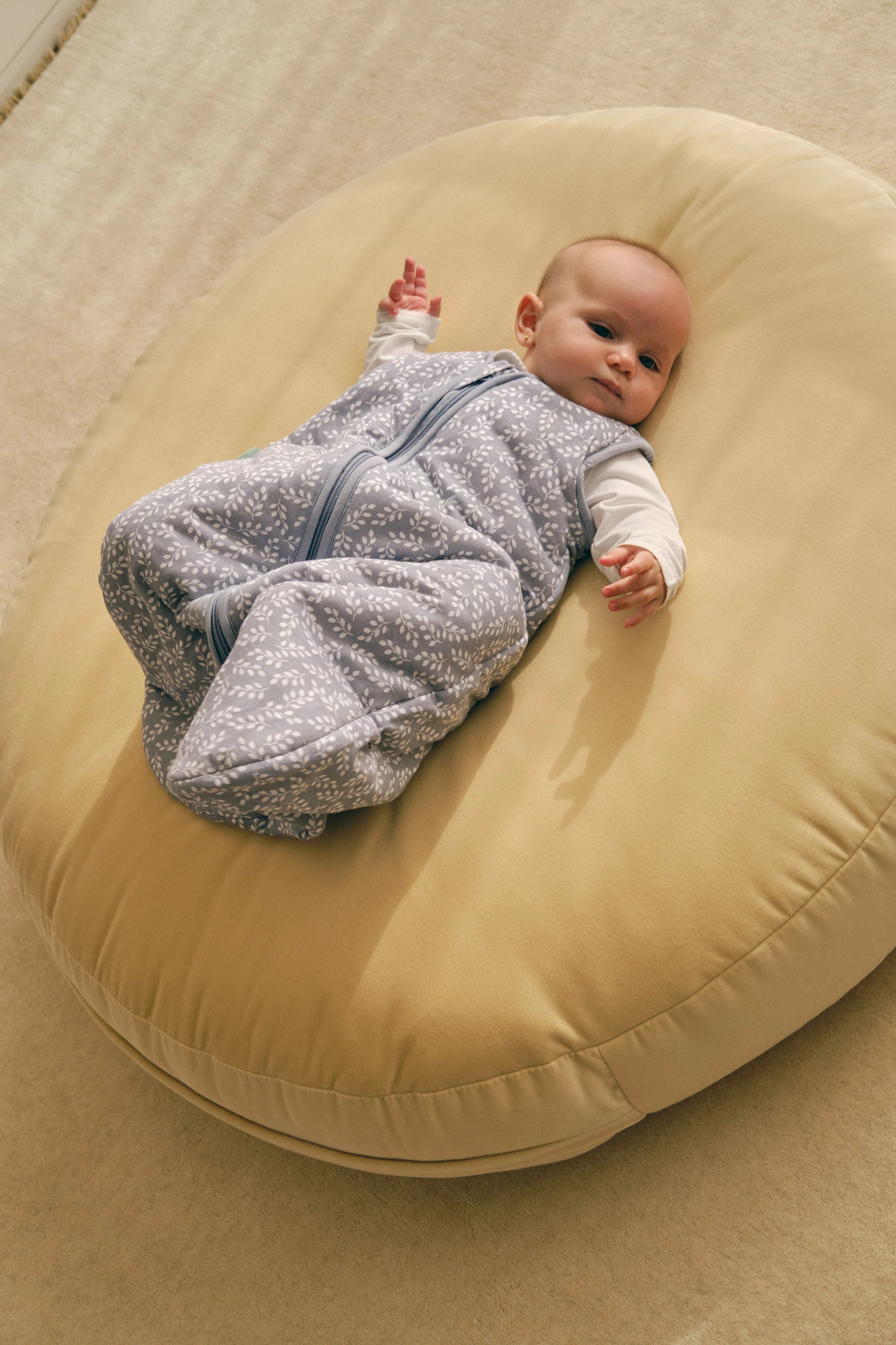 Bebé deitado num pufe, a usar o saco de dormir MolisandCo TOG 2.5 Blue Garden, mostrando conforto e design.